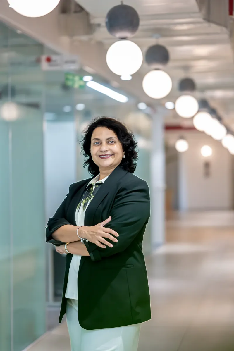 Mahua Gorthi, standing with her arms crossed, in a dark blazer.