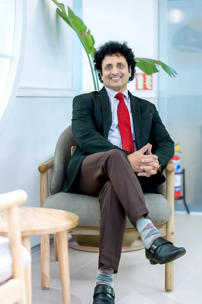 Venu Gorthi, seated in an armchair, in a dark blazer and red tie.